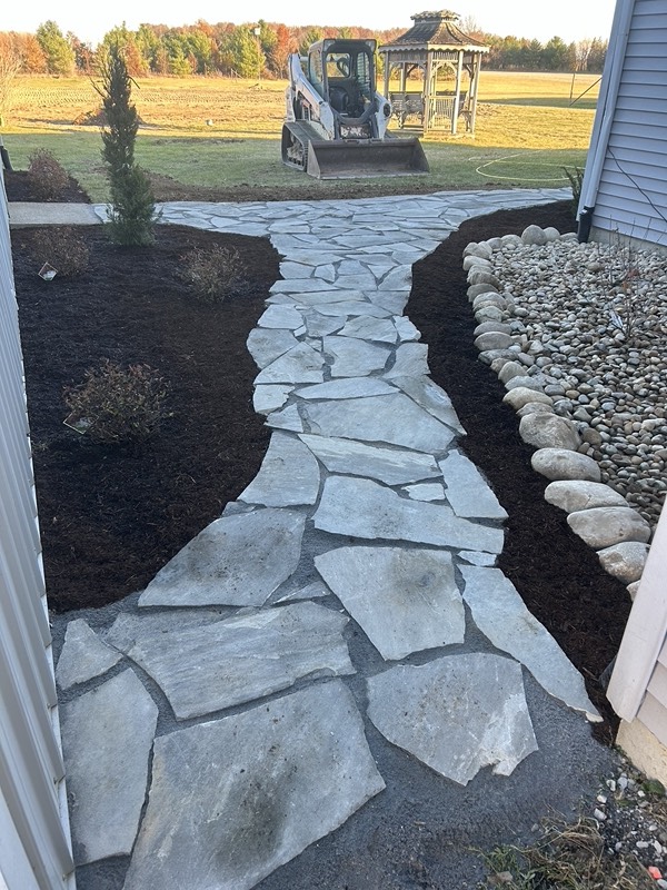 Natural flagstone walkway set between fresh mulch beds and a river rock border