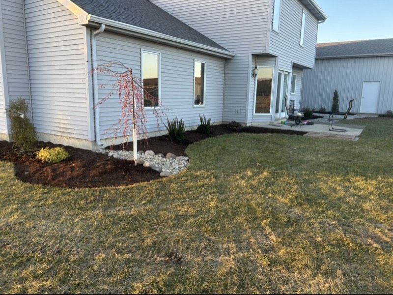 Curved mulch bed with river rock accents and a young weeping tree