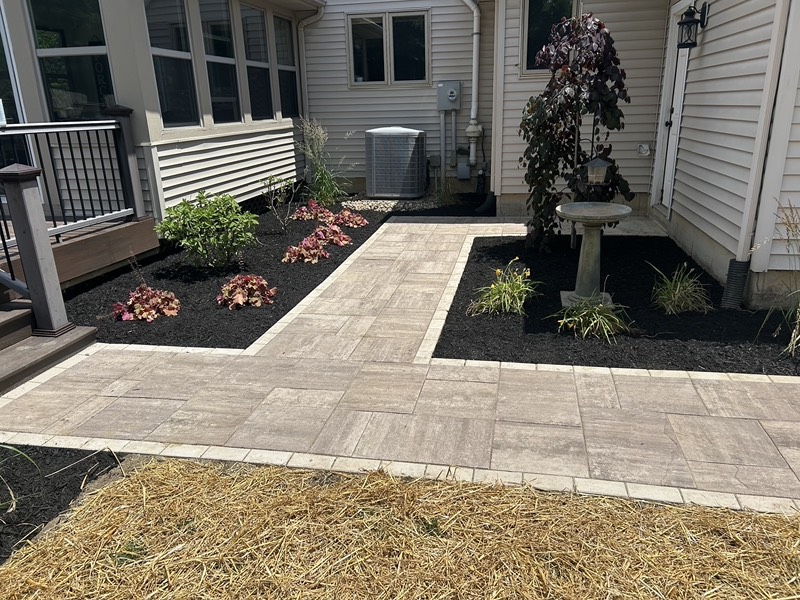 Freshly mulched planting beds on both sides of a light gray paver walkway